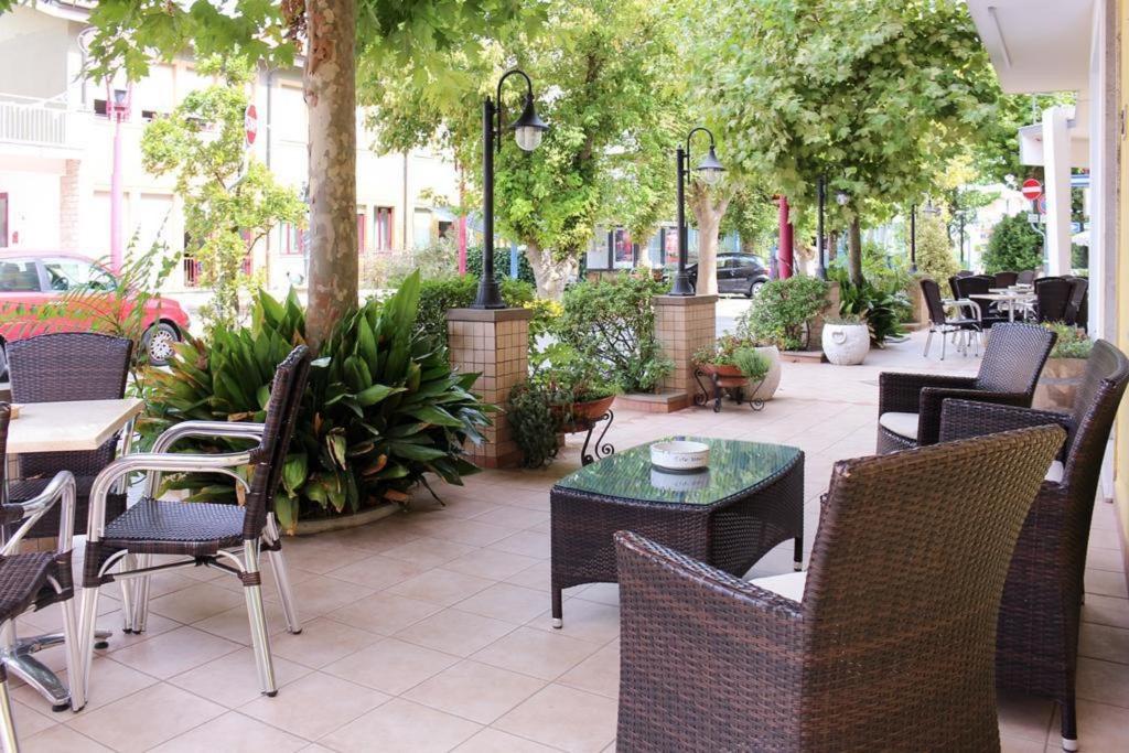 Un patio al aire libre con mesas, sillas y árboles. en Azzurro Beach Hotel Igea Marina, en Bellaria-Igea Marina