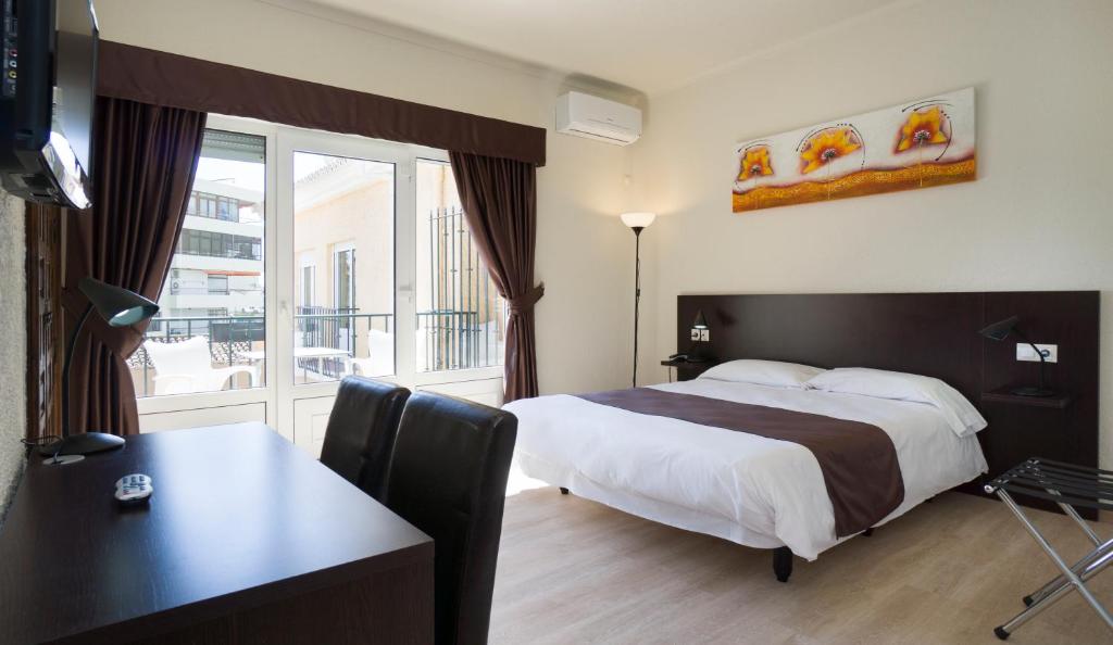 トレモリノスにあるHotel El Pozoのベッド、デスク、窓が備わるホテルルームです。