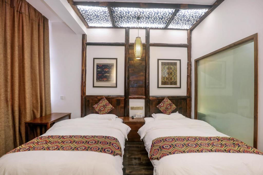 two beds in a room with white sheets and a window at 张家界畔山驿栈 in Zhangjiajie
