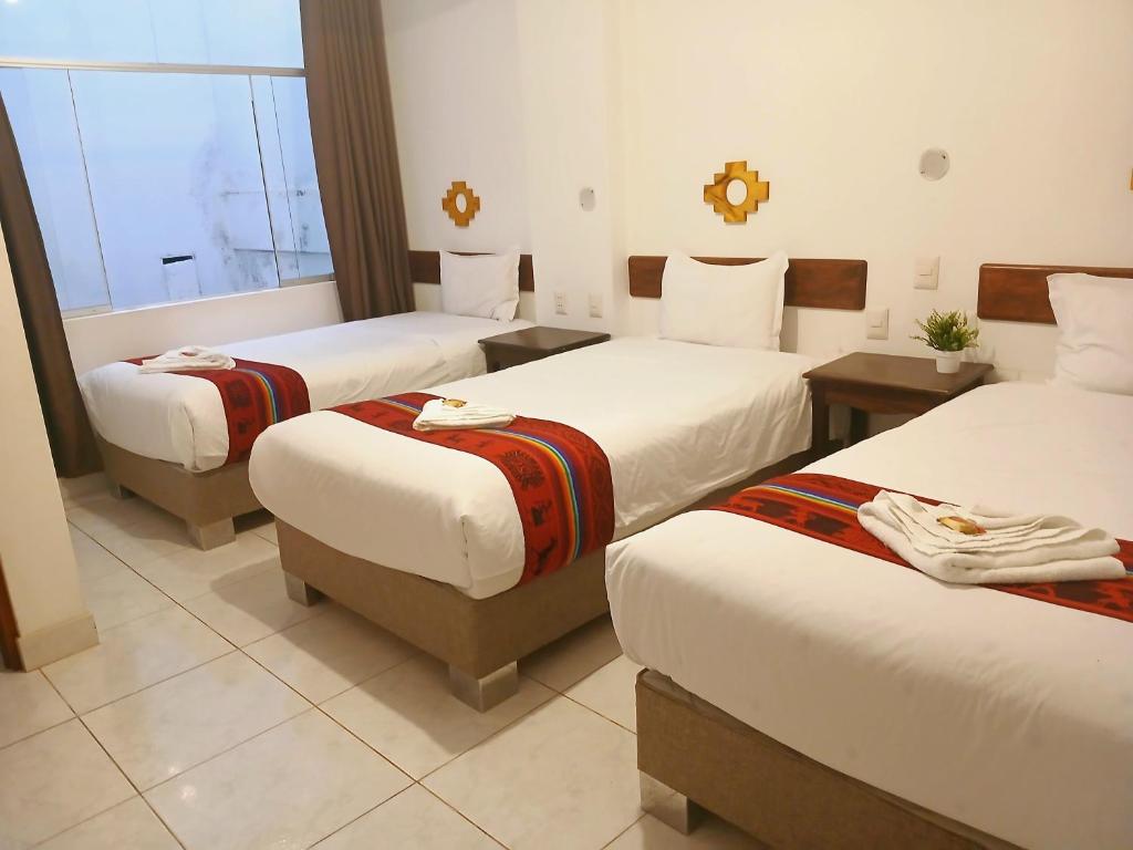 una camera d'albergo con tre letti e una finestra di PAKARINA HOTEL a Machu Picchu