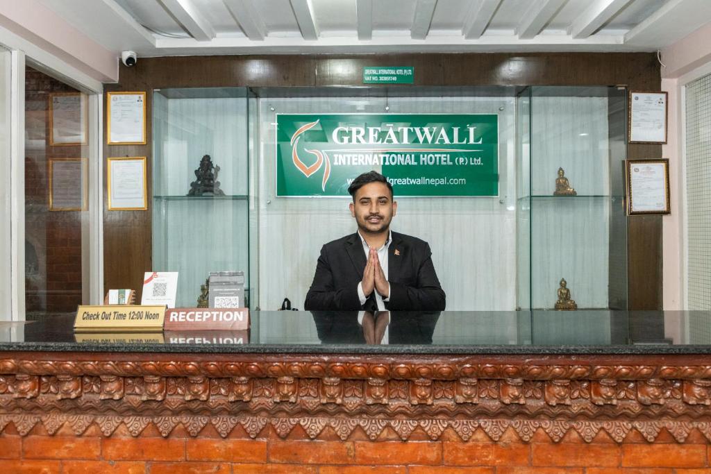 un hombre está sentado en un escritorio en una habitación en Greatwall International Hotel, en Katmandú
