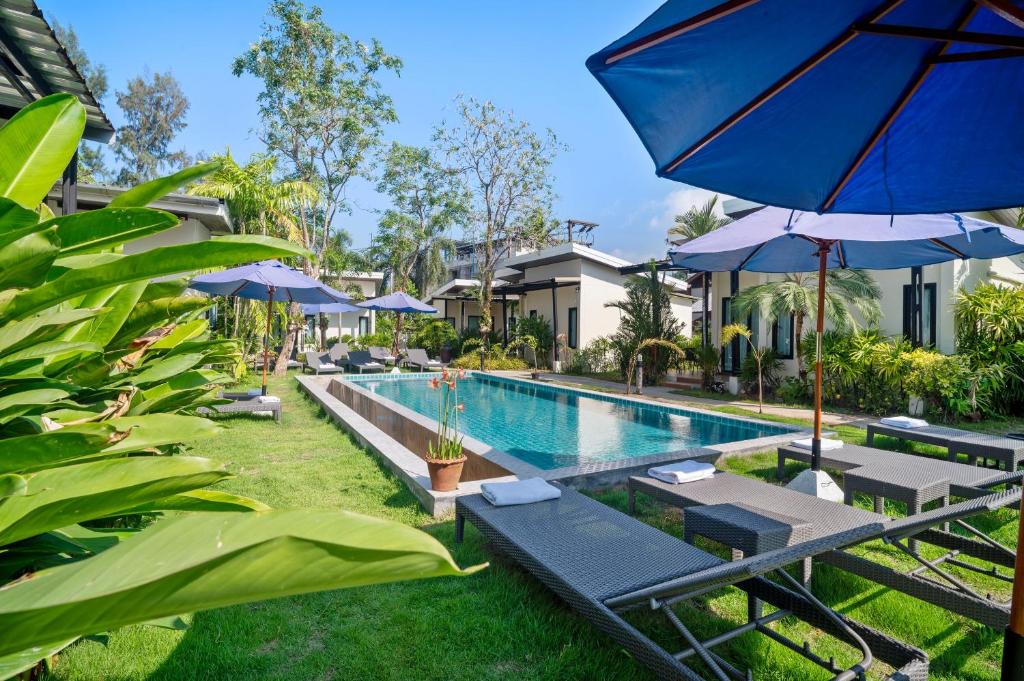 a pool with chairs and umbrellas next to a resort at La Casa Bangtao Resort in Ban Thalat Choeng Thale