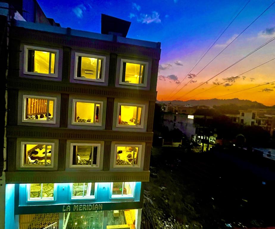 un edificio con ventanas iluminadas con la puesta de sol en el fondo en Hotel LA Meridian - Rishikesh Road, Haridwar, en Rishīkesh