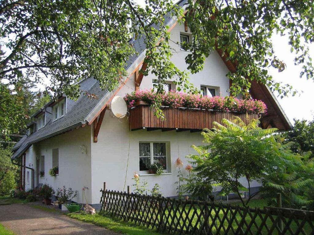 Cette maison blanche dispose d'un balcon fleuri. dans l'établissement Ferienwohnung Schartenschmiede, à Sankt Georgen im Schwarzwald