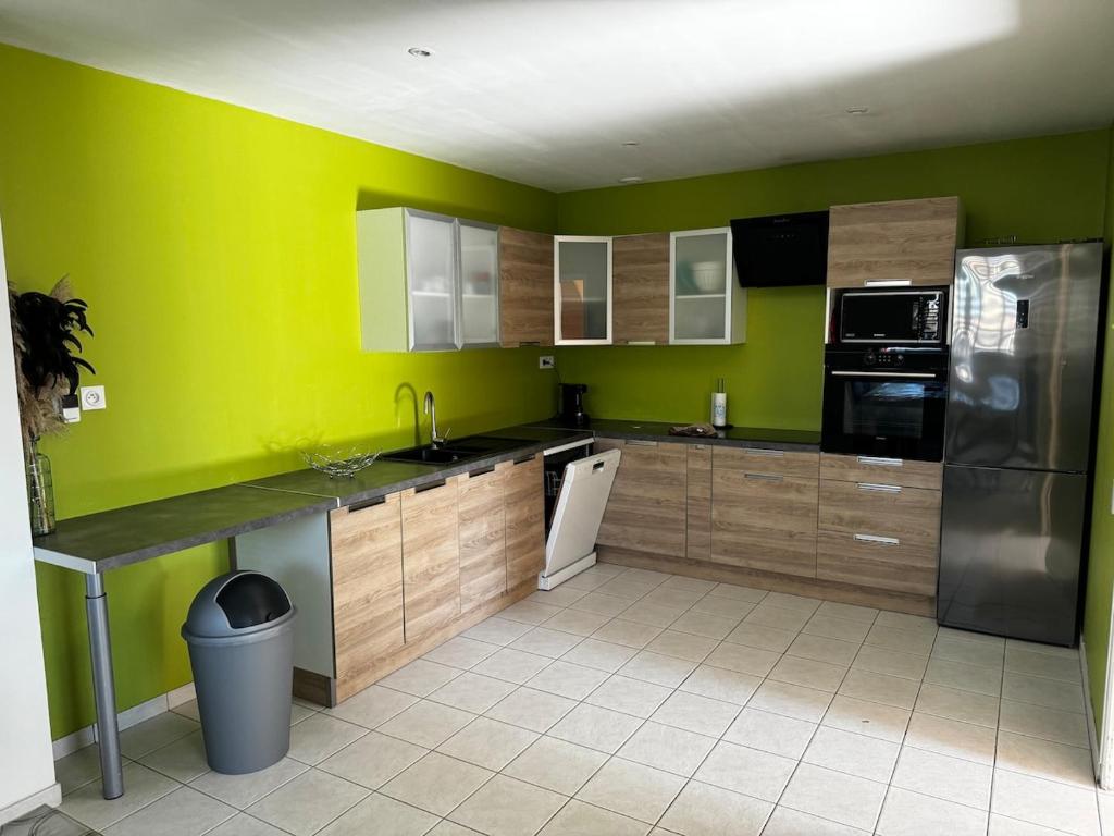 a kitchen with green walls and wooden cabinets at Maison proche de la plage et du CNPE in Oye-Plage