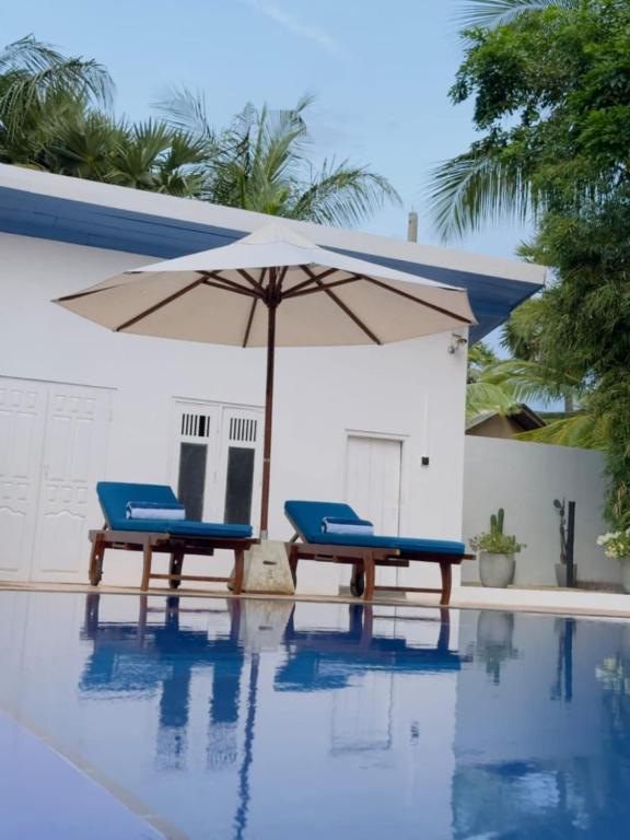 two chairs and an umbrella next to a swimming pool at Blue Kite Retreat in Kalpitiya