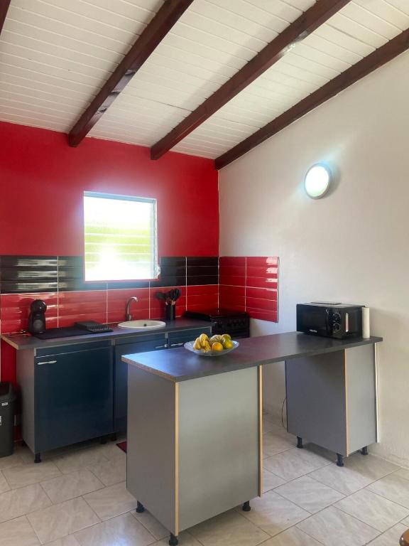 a kitchen with red walls and a table with a bowl of fruit at Gîte Le Géranium in Deshaies