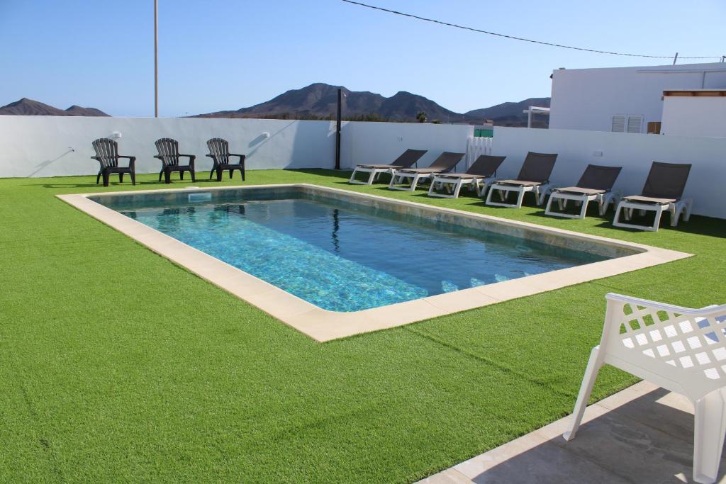 a swimming pool on a lawn with chairs around it at Fuerte Roche 2 in Tuineje