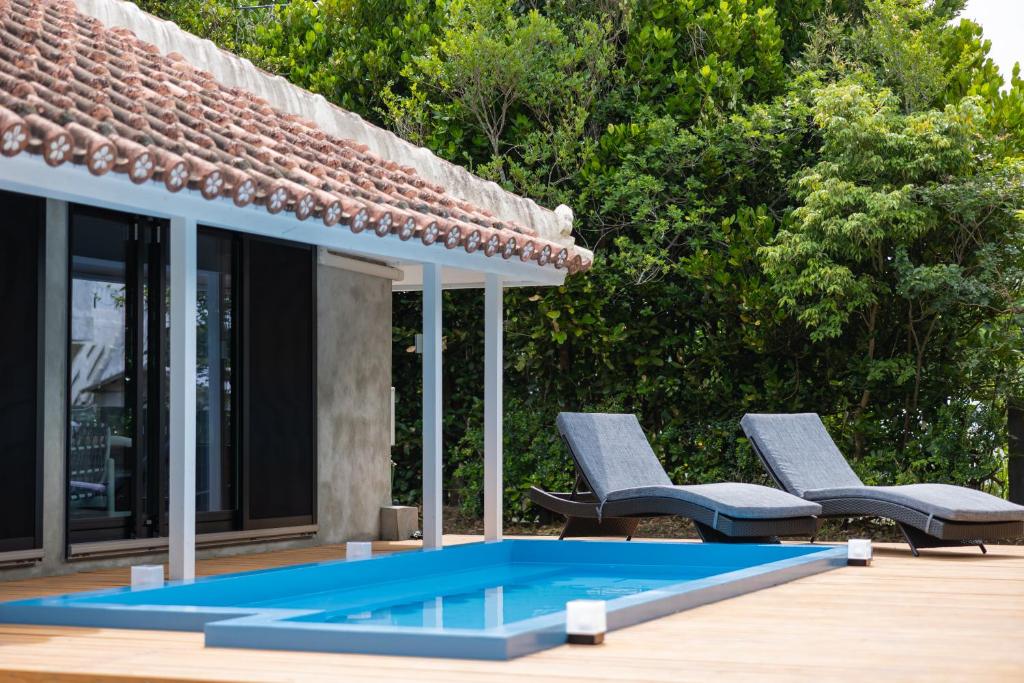 a swimming pool next to two chairs and a house at Tida Sesoko in Motobu