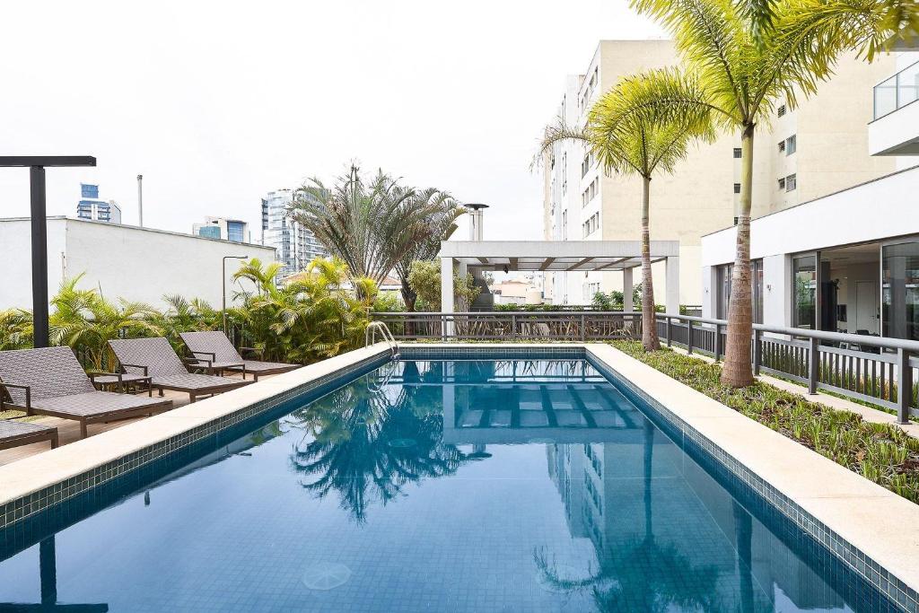 une piscine avec des palmiers et un bâtiment dans l'établissement Homelike by Viva - Apartamentos completos em Pinheiros a uma quadra da Faria Lima, à São Paulo