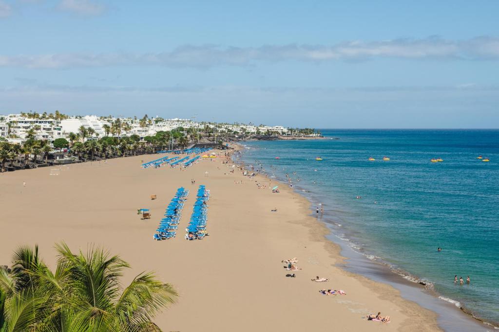 a beach with blue umbrellas and people on it at Plus Fariones Suite Hotel in Puerto del Carmen