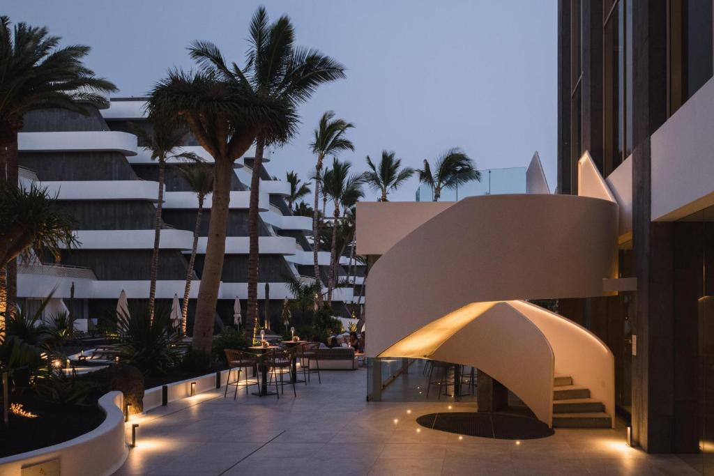 an outdoor patio with palm trees and a building at Plus Fariones Suite Hotel in Puerto del Carmen