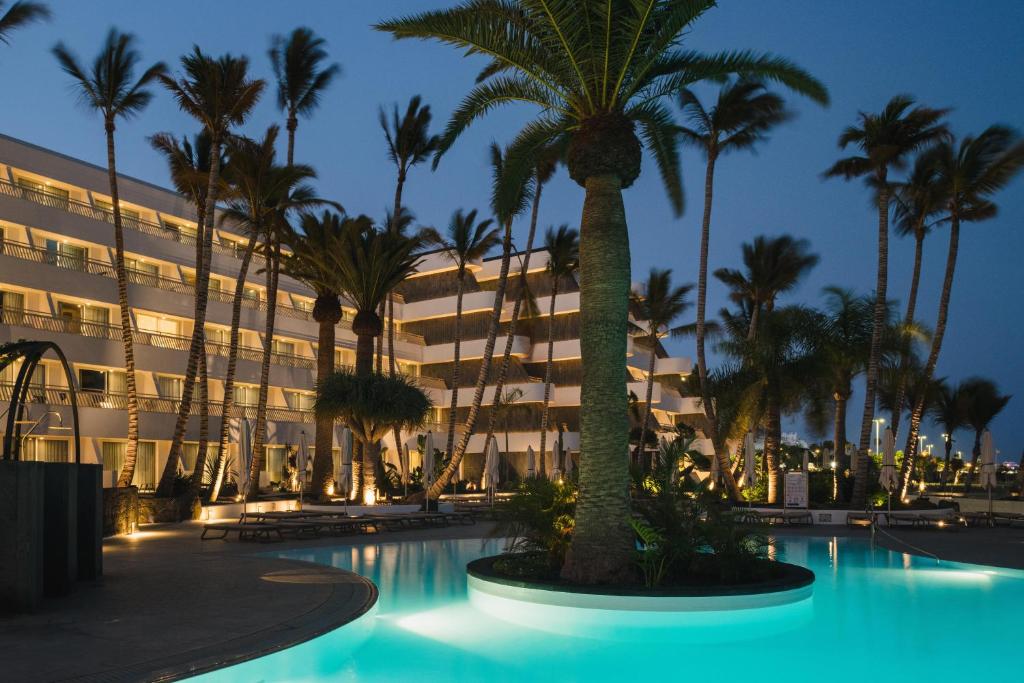 a hotel with palm trees in front of a building at Plus Fariones Suite Hotel in Puerto del Carmen