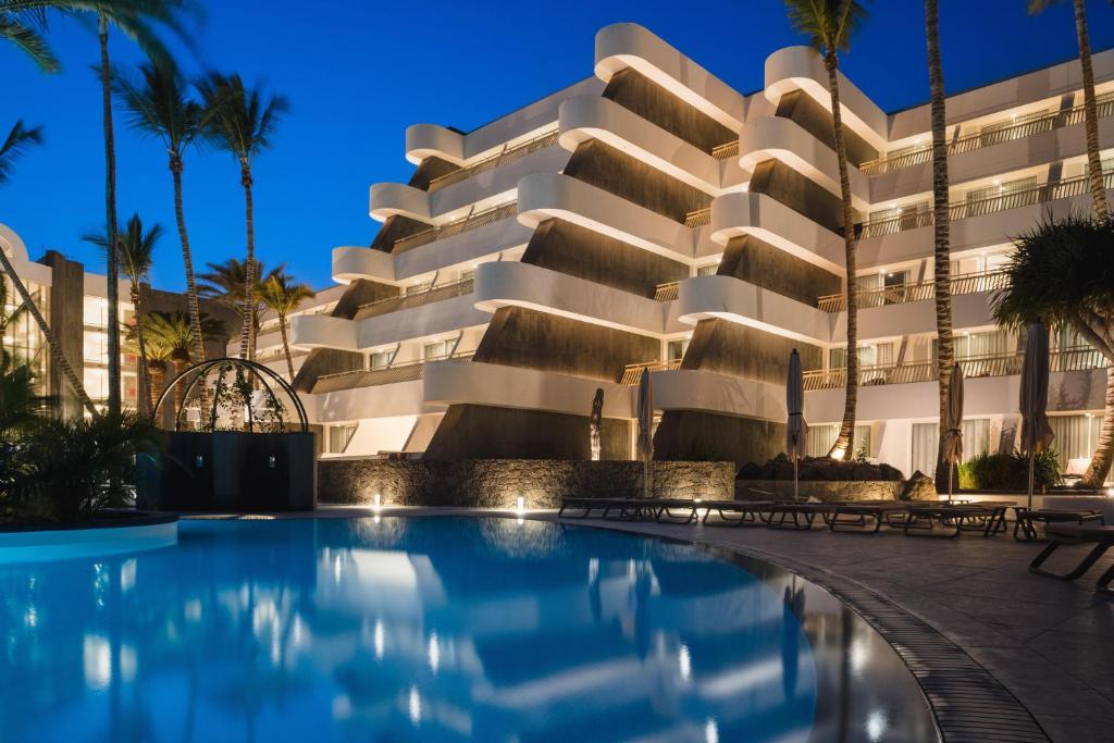 a hotel with a swimming pool in front of a building at Plus Fariones Suite Hotel in Puerto del Carmen