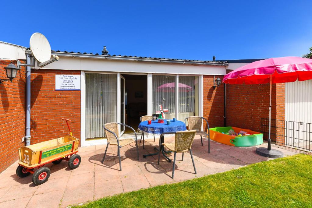 um pátio com uma mesa, cadeiras e um guarda-sol em Strandnahes Ferienhaus Mit Kinderspielplatz em Esens