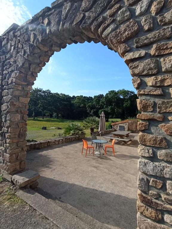 une arche dans un mur en pierre avec une table et des chaises dans l'établissement Auberge des Quatre Moulines, à Le Longeron