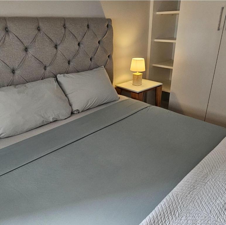 a bed with a gray headboard and a table with a lamp at COZY APARTMENT, 1 HAB, Piscina, ZONA Shopping del Sol in Asuncion