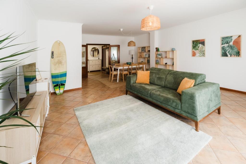 a living room with a green couch and a surfboard at Casa do Sargaço Moledo in Moledo