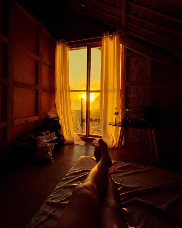 a person laying on a bed looking out a window at A-Frame Cottage 2, Puraran Surf Resort in Baras
