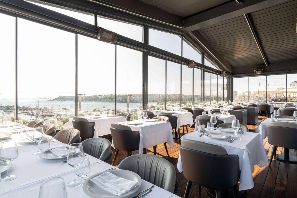 a restaurant with white tables and chairs and windows at Wyndham Grand Istanbul Kalamış Marina Hotel in Istanbul