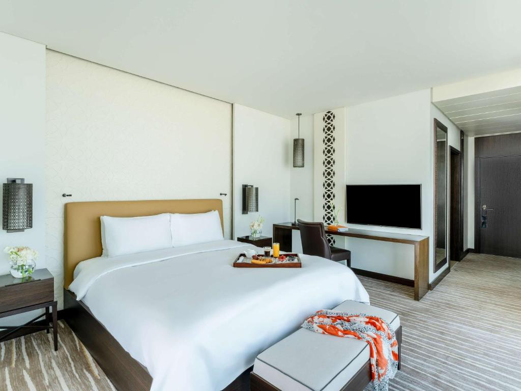 a hotel room with a large bed and a television at Alwadi Hotel Doha - MGallery Collection in Doha