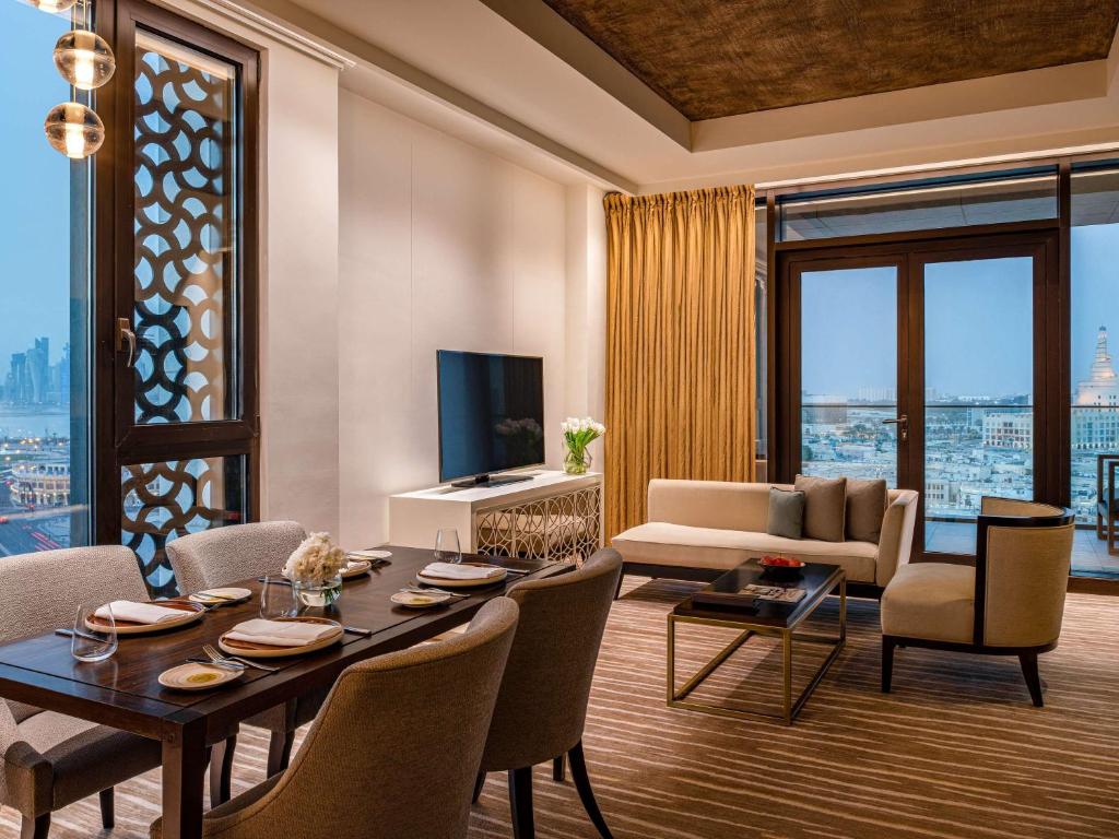 a living room with a table and chairs and a television at Alwadi Hotel Doha - MGallery Collection in Doha