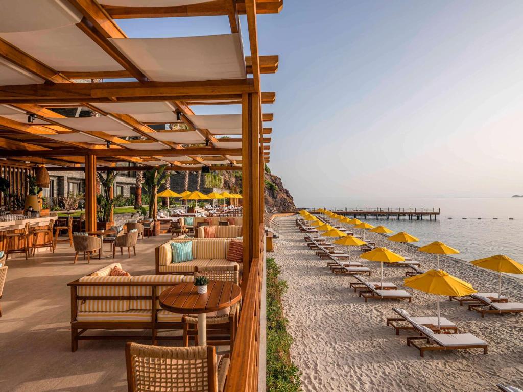 a beach with chairs and tables and umbrellas at The Bodrum Hotel Yalikavak - MGallery Collection in Yalıkavak