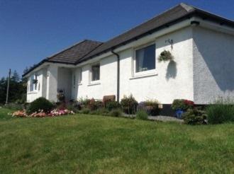 a white house with a green lawn in front of it at B&B Ronan House in Edinbain