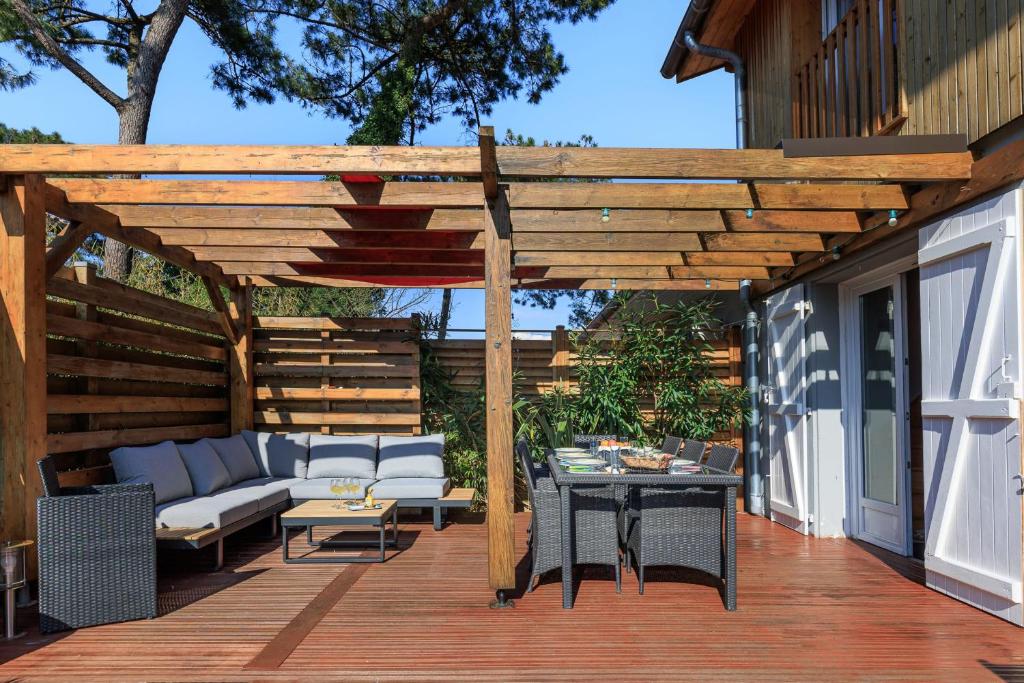 une pergola en bois avec un canapé et une table sur une terrasse dans l'établissement Maison des Bonheurs Océaniques - Welkeys, à Capbreton