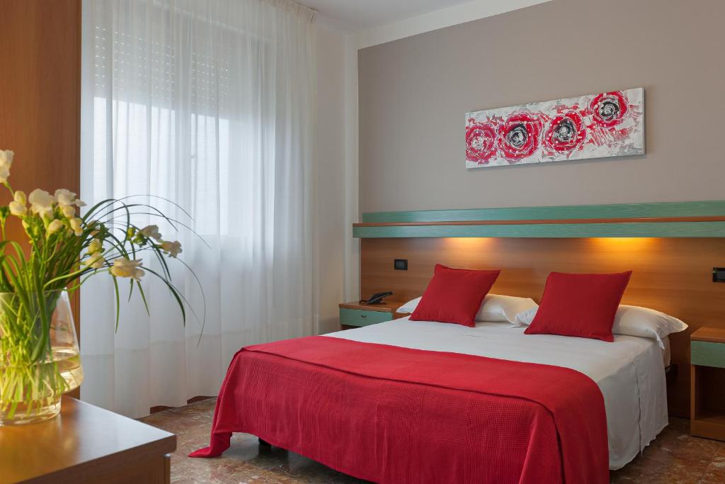 a bedroom with a bed with red sheets and a vase of flowers at Hotel Europeo in Sottomarina