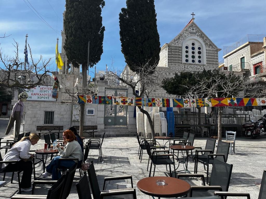 two people sitting at tables in front of a church at Kantouni house Chios in Pyrgi