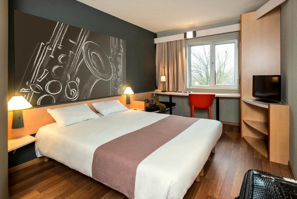 a hotel room with a large bed and a tv at ibis Dinant Centre in Dinant