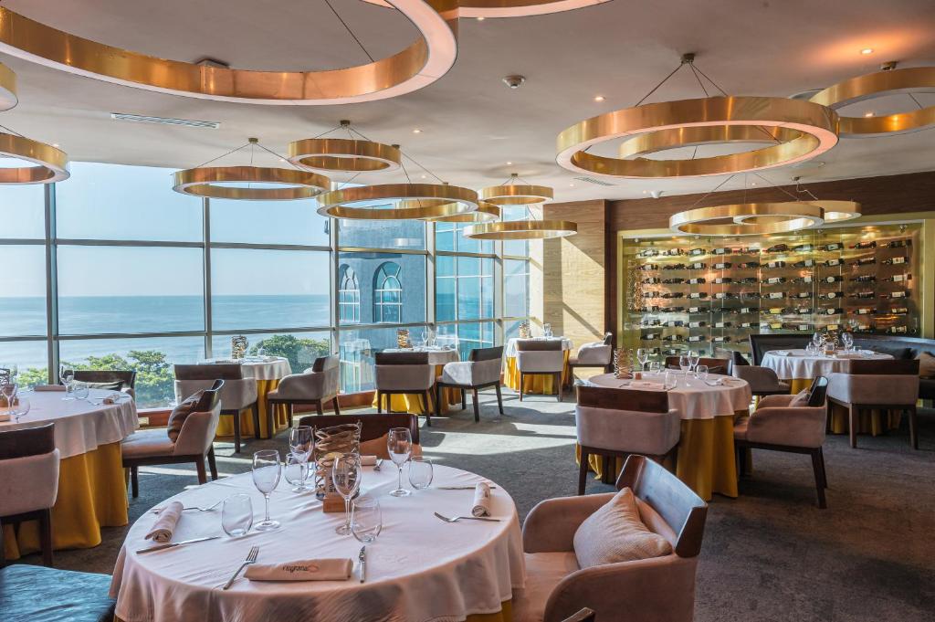 a restaurant with white tables and chairs and windows at Catalonia Santo Domingo in Santo Domingo