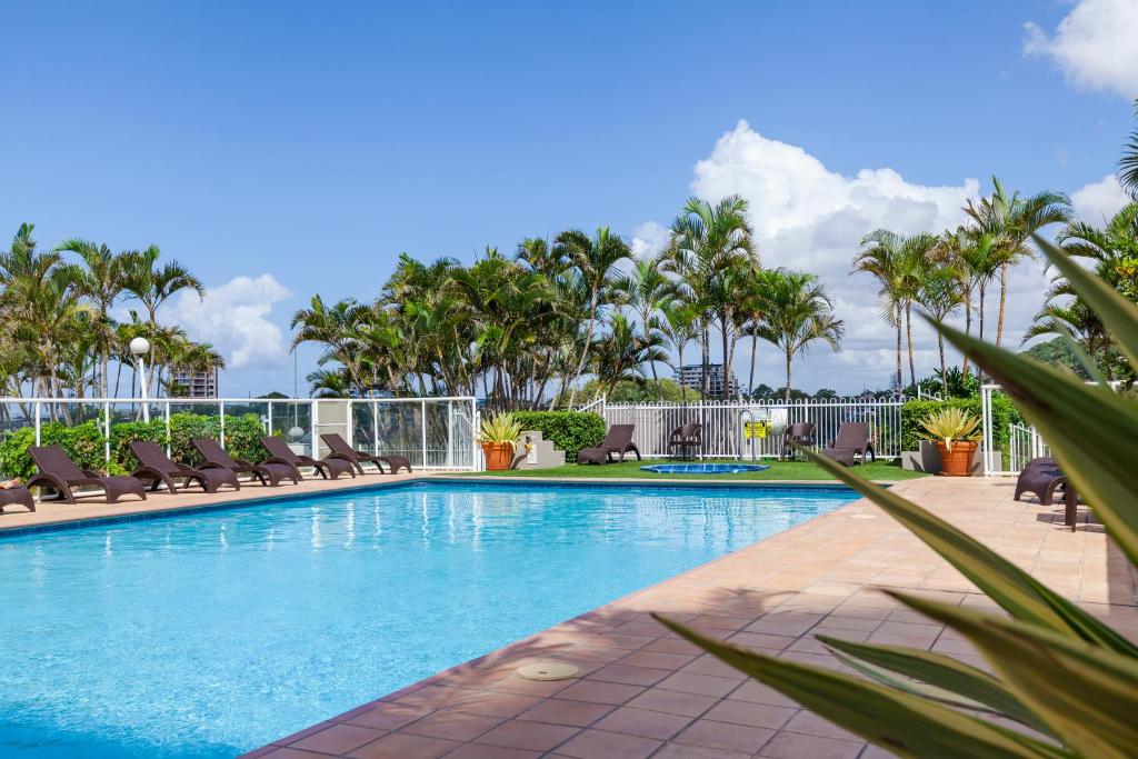 a swimming pool with lounge chairs and palm trees at Points North Apartments in Gold Coast
