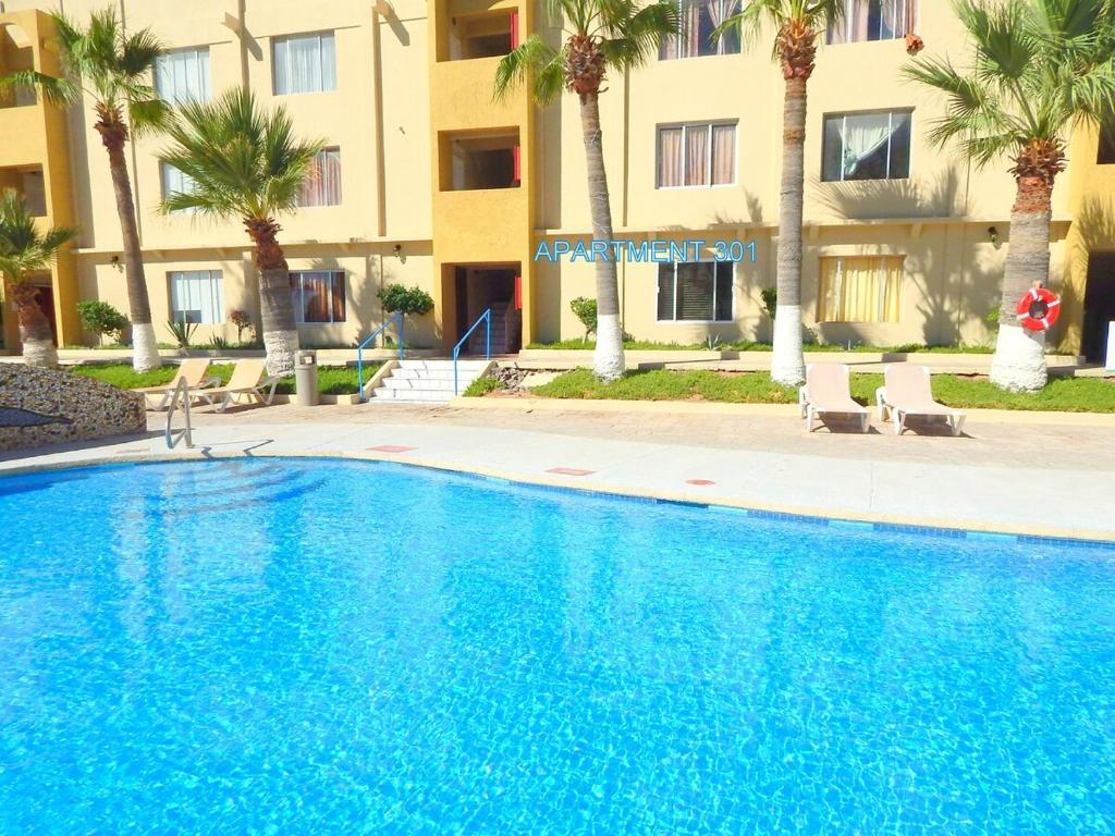 a swimming pool in front of a building with palm trees at Sea Breeze Retreat 301 in Puerto Peñasco