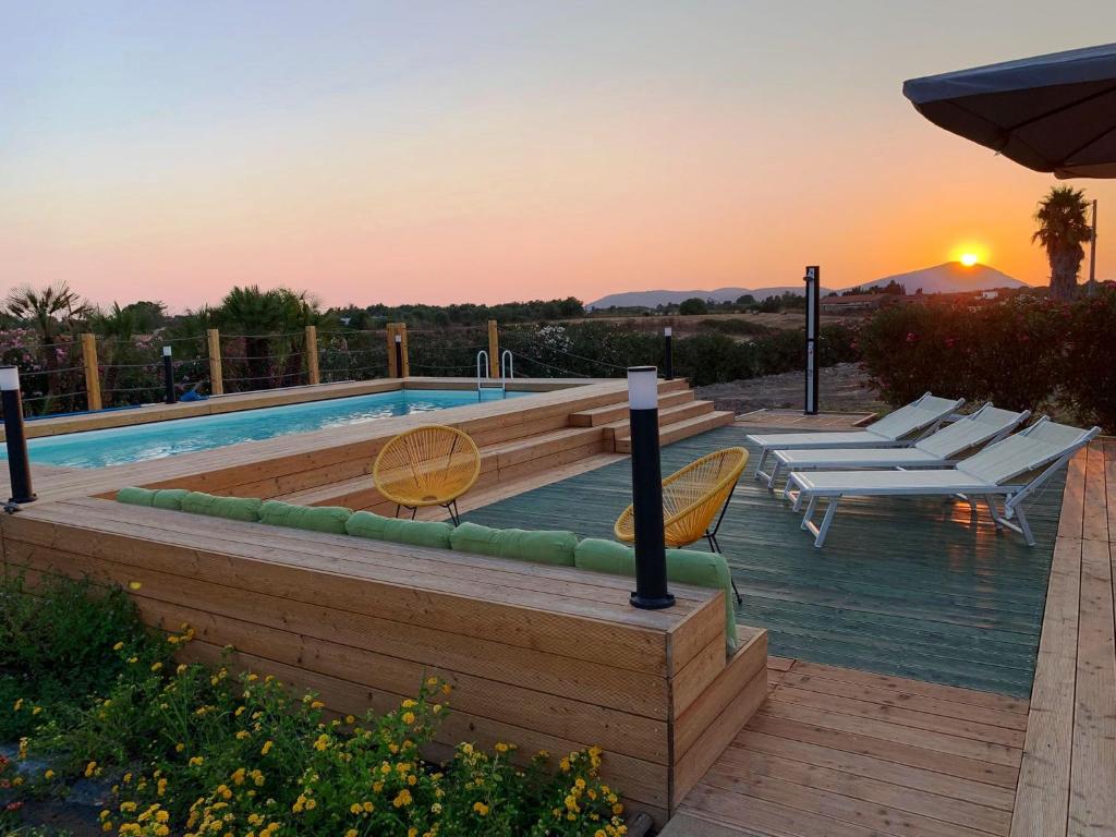 une piscine avec des chaises et un coucher de soleil en arrière-plan dans l'établissement Villa Blanc Country, à Alghero