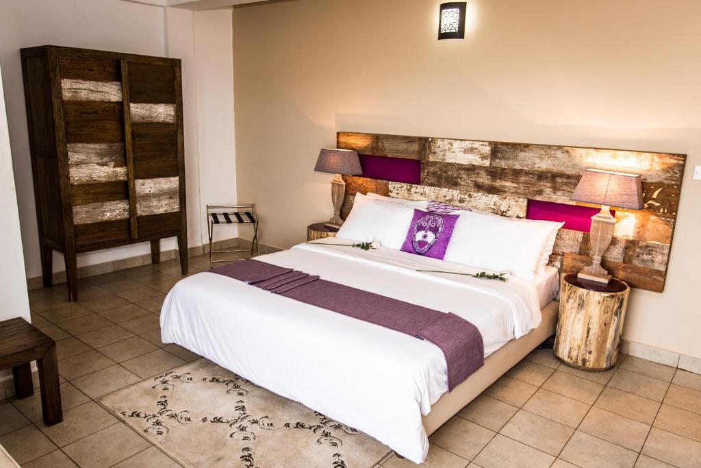 1 dormitorio con 1 cama blanca grande con toques morados en The Swiss Hotel Freetown, en Freetown