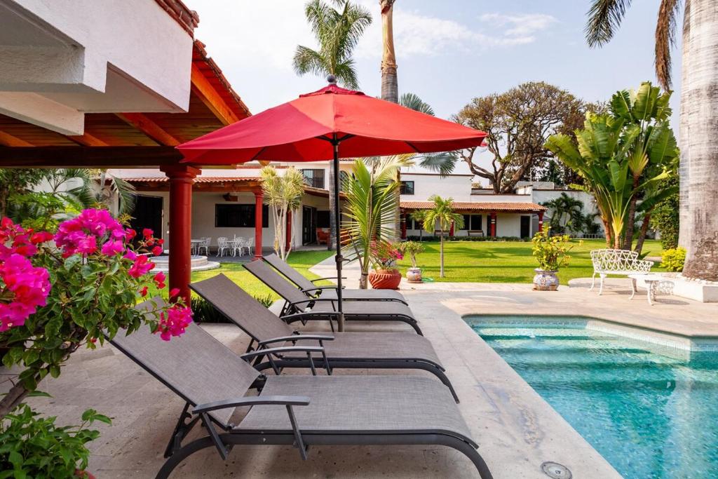 a row of chairs with an umbrella next to a pool at Villa MAJUM Cocoyoc in Cocoyoc