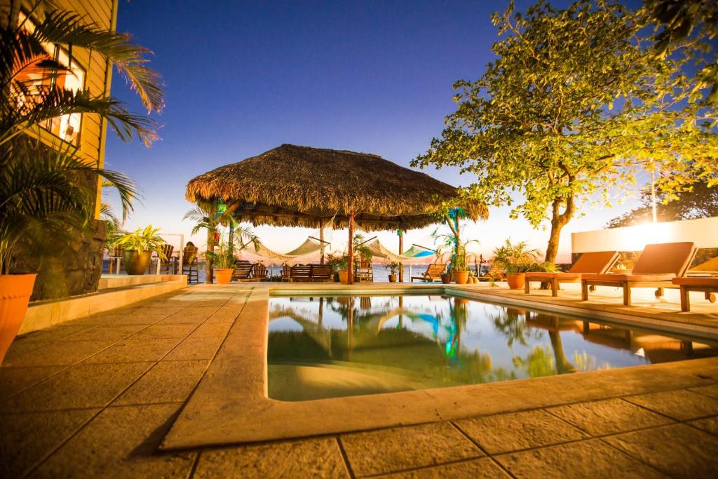 a swimming pool with benches and a straw umbrella at Casa la barra surf resort in Miramar