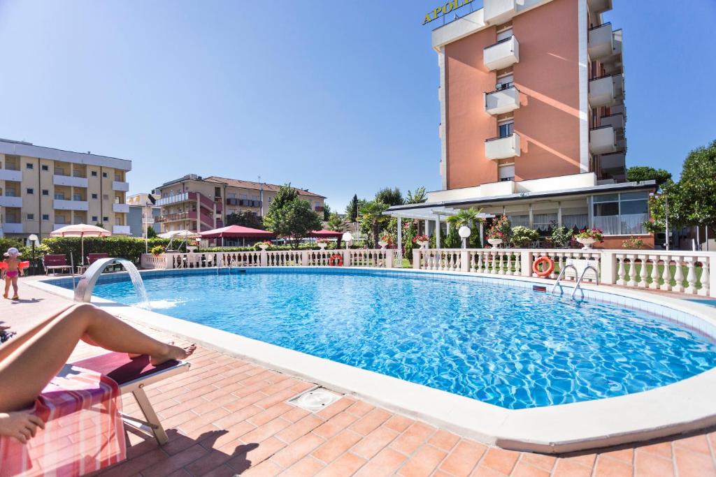 a woman sitting on a chair next to a swimming pool in a hotel at Hotel Apollo in Rimini