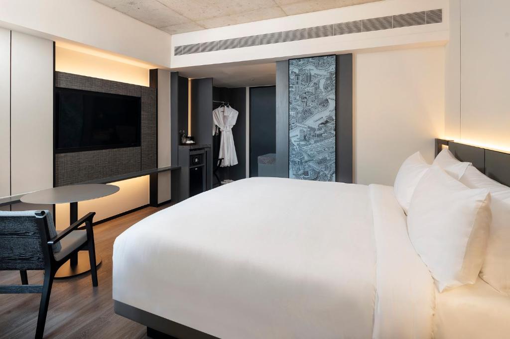 A modern guest room with a large bed, wall-mounted TV and compact dining-work table.