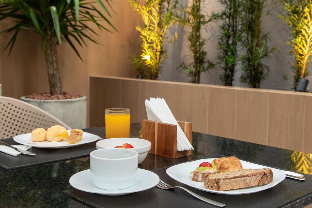 a table with two plates of food and a cup of orange juice at Slim Curitiba Alto da XV in Curitiba