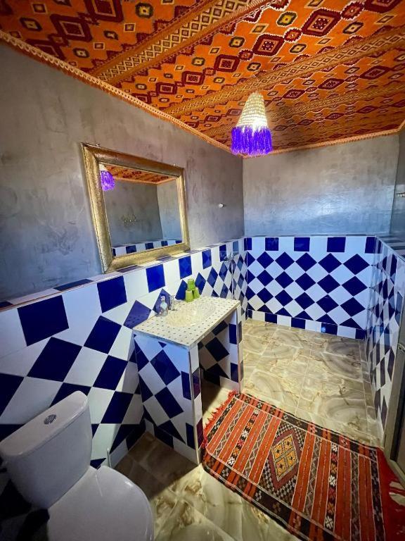 un bagno bianco e blu con servizi igienici e specchio di Chigaga Desert Camp a M'Hamid