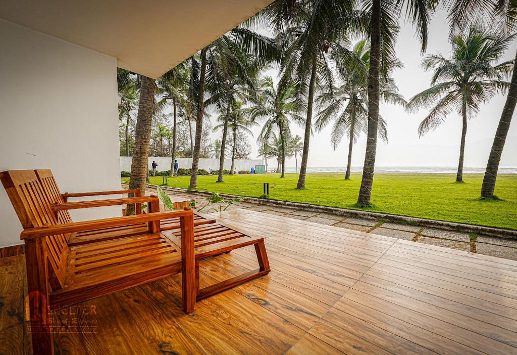 a wooden bench sitting on a porch with palm trees at Shelter Beach Resort in Mahabalipuram