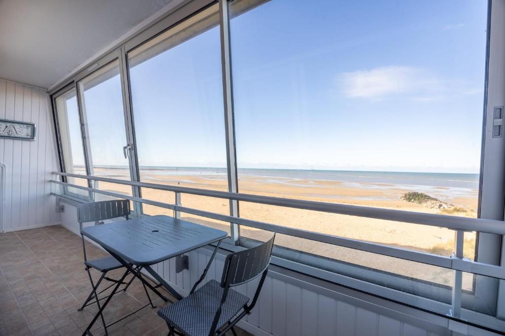 une table et des chaises sur un balcon avec vue sur la plage dans l'établissement Les Marinas front of the beach, à Courseulles-sur-Mer