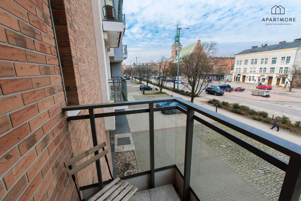 Corner balcony with wooden chair, glass railing and brick wall, overlooking city street and church steeple.