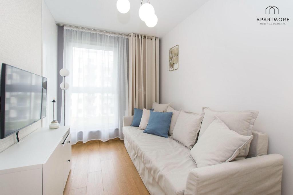Cozy narrow sitting room with white sofa, multiple cushions, wall TV and soft lighting.
