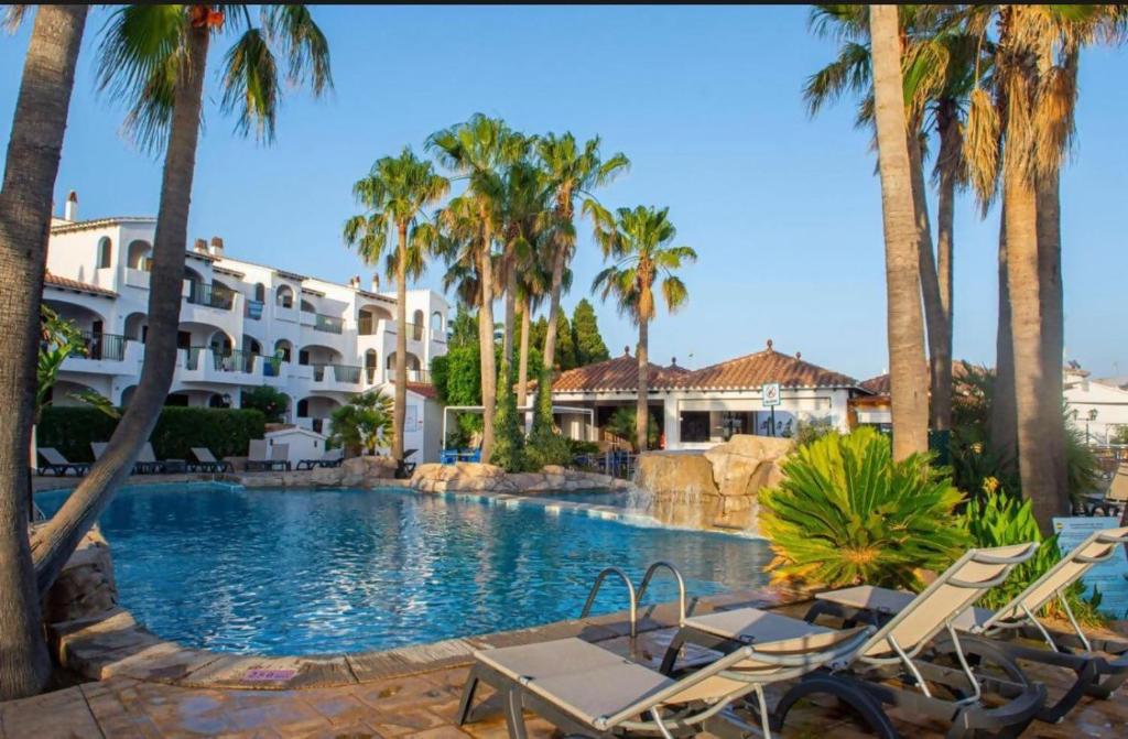 a resort swimming pool with chairs and palm trees at Oasis Calan Porter con piscinas y junto la playa in Cala'n Porter
