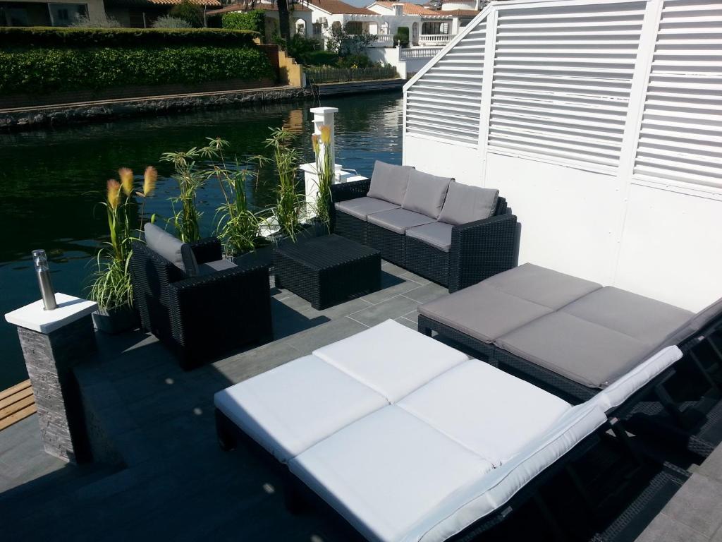 a patio with two couches and chairs next to the water at Villa des Pecheurs in Empuriabrava