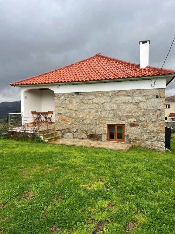 a stone house with a red roof on a green field at Casa do Cascalho in Ribeira de Pena
